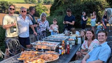 Un grupo de personas reunidas alrededor de una mesa con comida y bebidas, al aire libre con una vista panorámica de fondo.