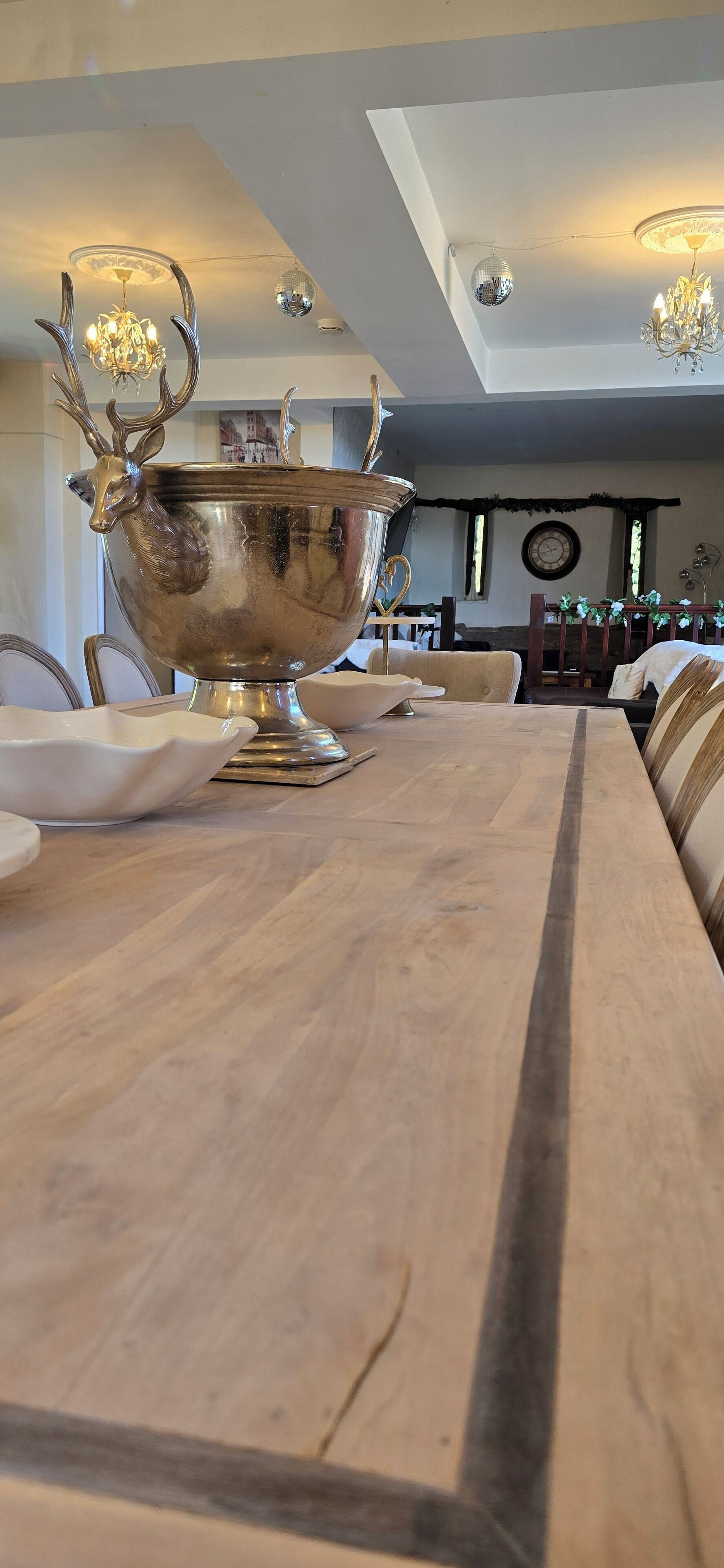 A dining table with a large silver bowl and a chandelier above.