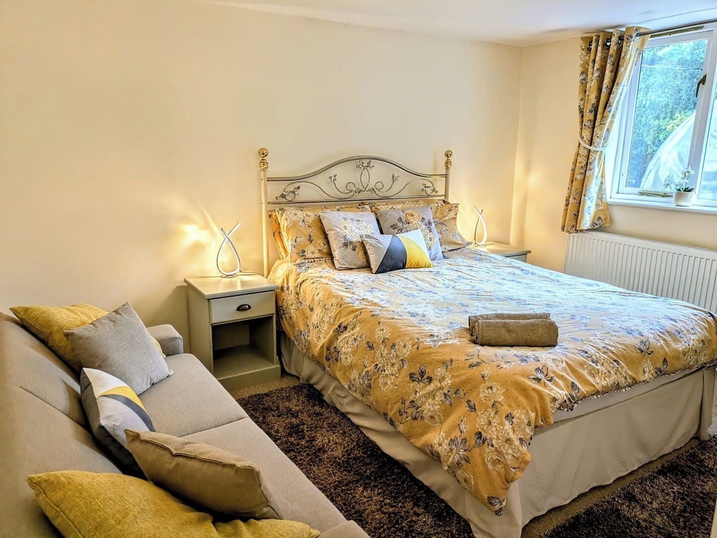 Un dormitorio con una cama, mesitas de noche, un sofá y una ventana con cortinas.