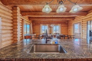 Ein Interieur einer Blockhütte mit einem Waschbecken aus Granit, Holzwänden, einem Essbereich mit Stühlen und einer Kristallleuchtre.