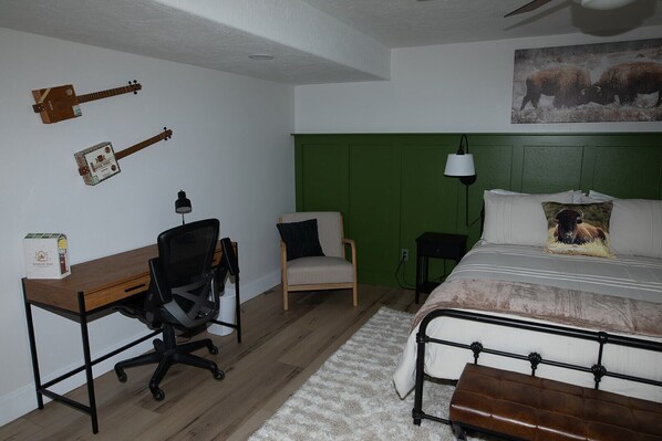 A bedroom with a bed, a desk, a chair, a lamp, and wall decorations including a guitar and a painting of bison.