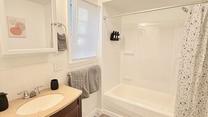 A bathroom with a sink, mirror, towel rack, shower, and toilet. - Luxe charming  2-bedroom apartment in Rochester (Rochester)