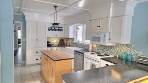 Une cuisine moderne avec des meubles blancs, un îlot central en bois, un four à micro-ondes et un dosseret carrelé.