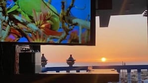 Une chambre dotée d’un téléviseur diffusant des images de la nature, d’un balcon offrant une vue sur le coucher de soleil et d’une lanterne de style traditionnel.