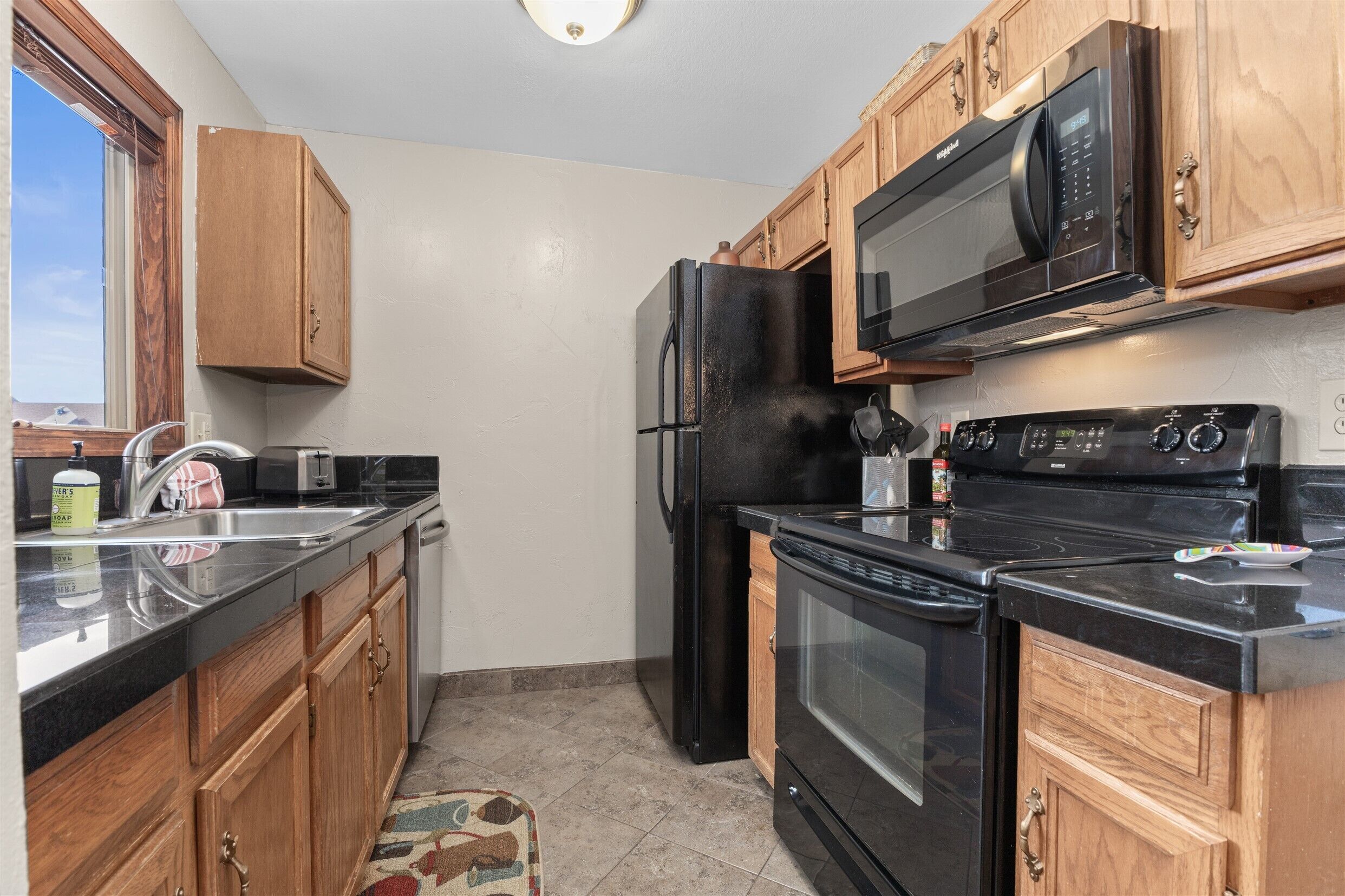 A kitchen with wooden cabinets, a black refrigerator, a microwave, a stove, and a sink.