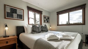 Ein Schlafzimmer mit einem großen Bett, zwei Nachttischen, einer Lampe und gerahmten Kunstwerken an den Wänden.