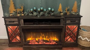 Una chimenea con repisa decorada con piñas y ramas de hoja perenne, y un control remoto encima.