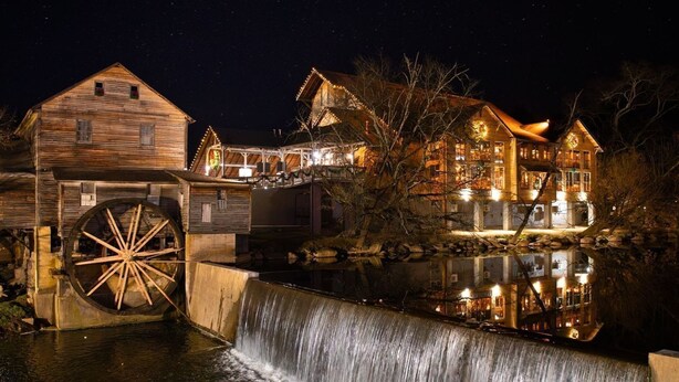 Un bâtiment historique doté d’une grande roue à eau, d’une façade en bois et de fenêtres illuminées la nuit.