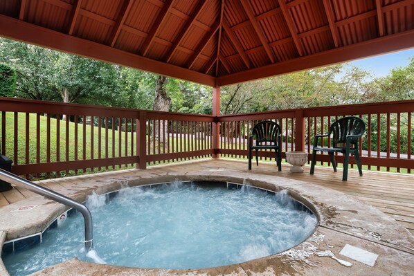 A hot tub with a wooden deck and railings, surrounded by greenery.