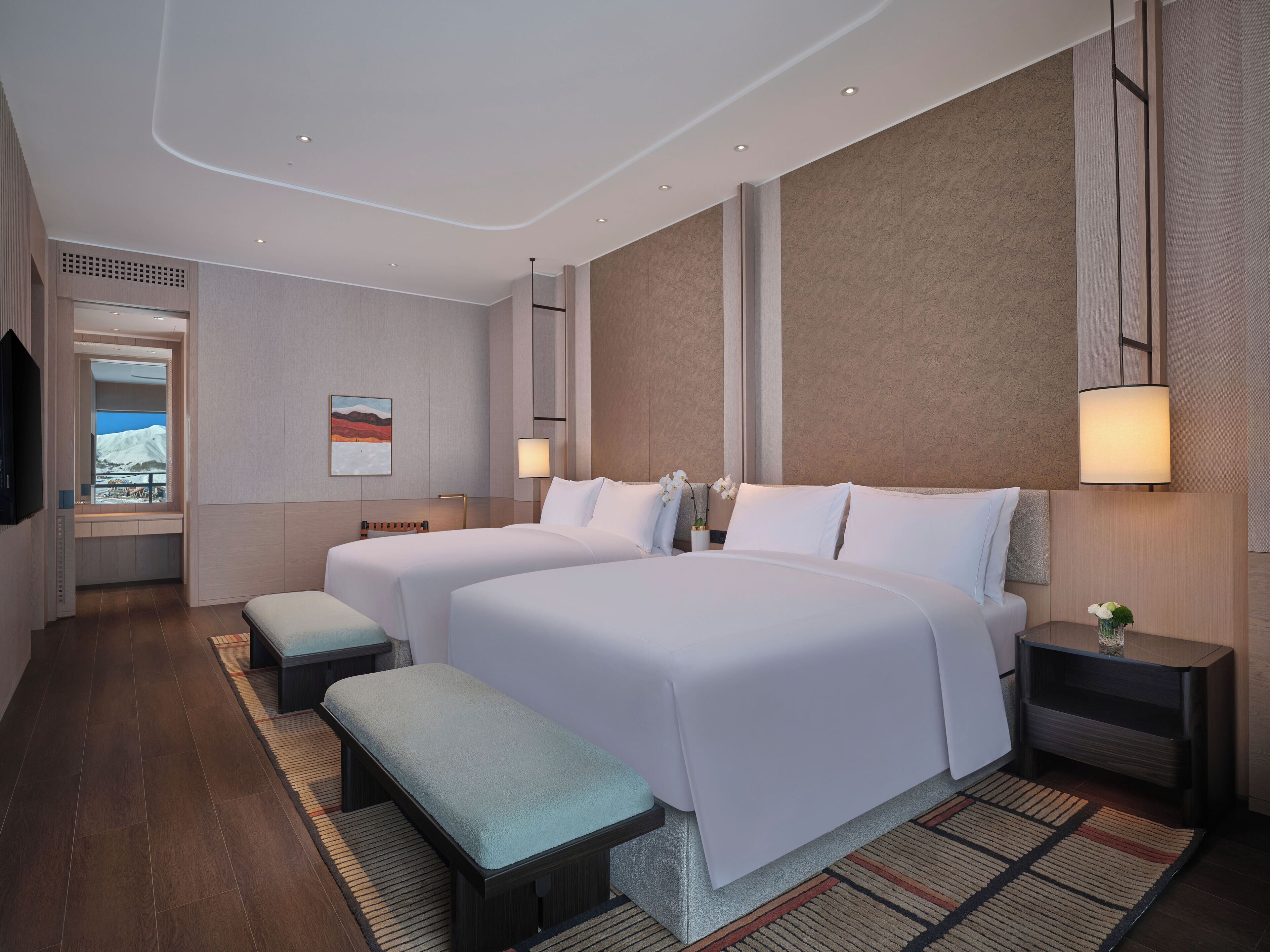 Une chambre d’hôtel moderne avec deux lits, un banc, une télévision et une vue sur un paysage enneigé.