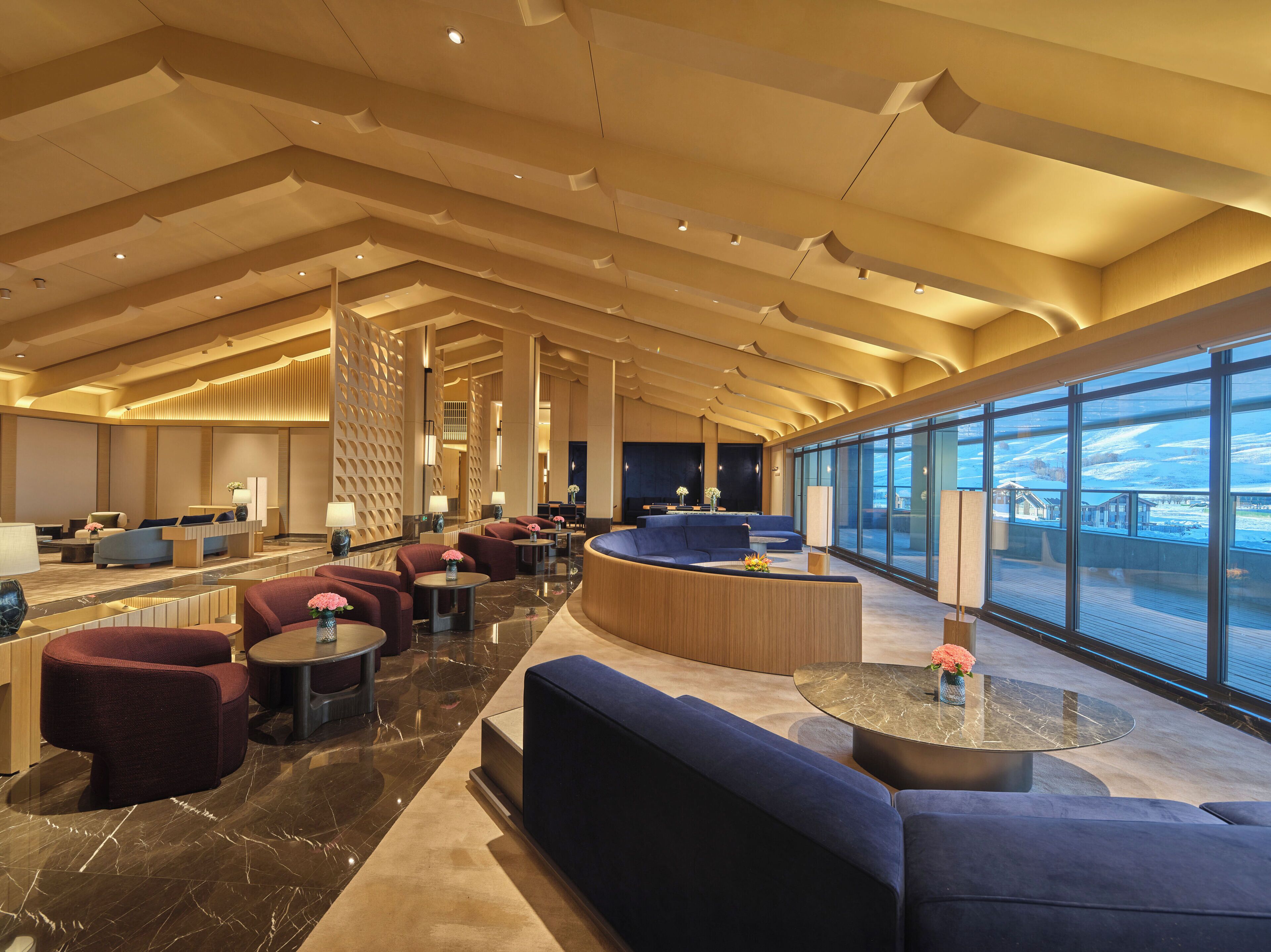 A spacious lobby with a high ceiling, marble flooring, and a seating area with sofas and round tables.