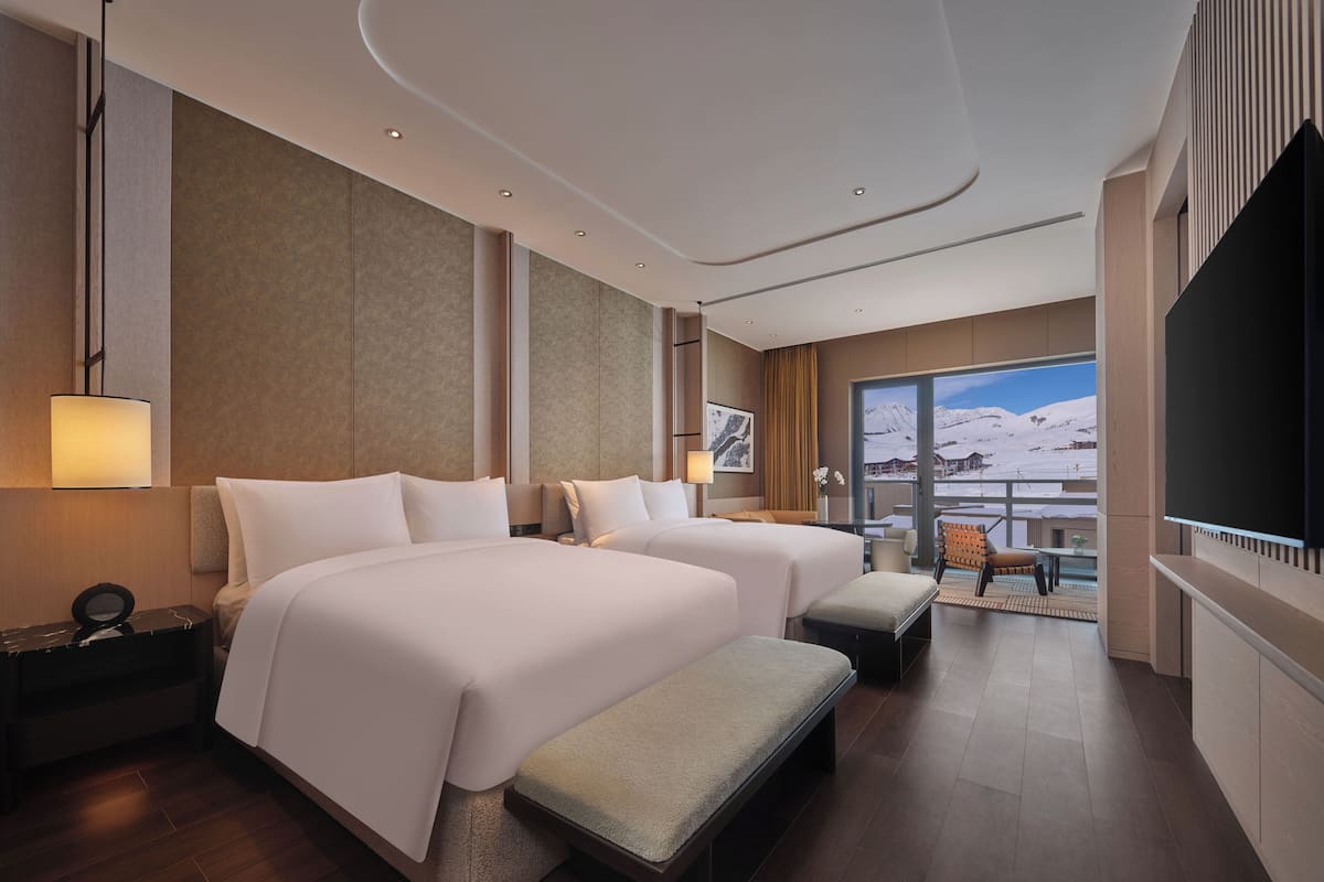Un hotel moderno con dos camas, un balcón con vistas a montañas nevadas y un televisor de pantalla plana.