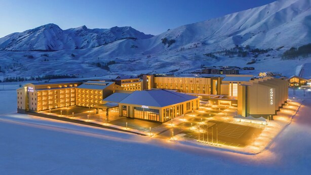 A snow-covered hotel with multiple buildings, a parking area, and a mountainous backdrop. - Conrad Altay Hemu (Burqin)