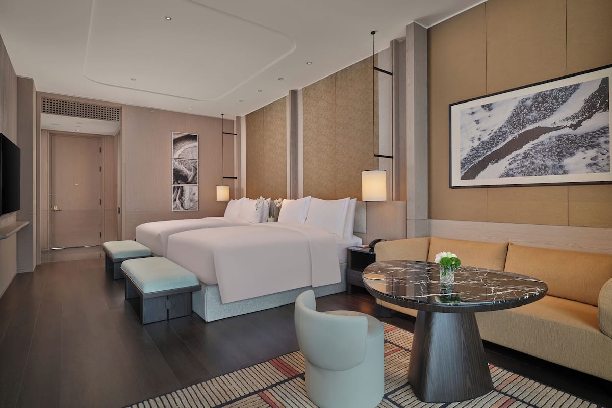 Una habitación de hotel moderna con una cama grande, un sofá, una mesa redonda de centro y un televisor montado en la pared.