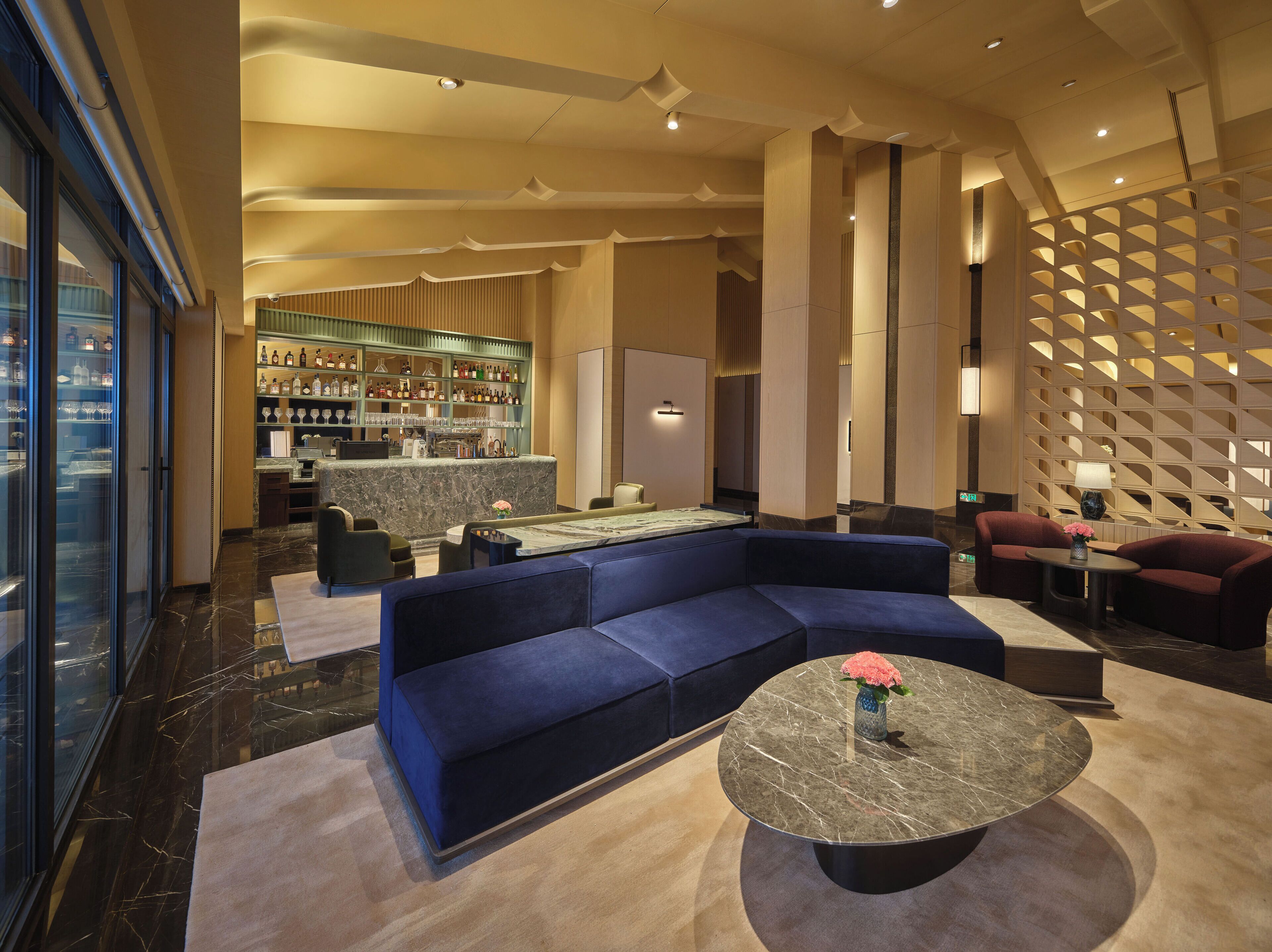 A modern hotel lobby with a bar area, seating arrangements, and a decorative wall.