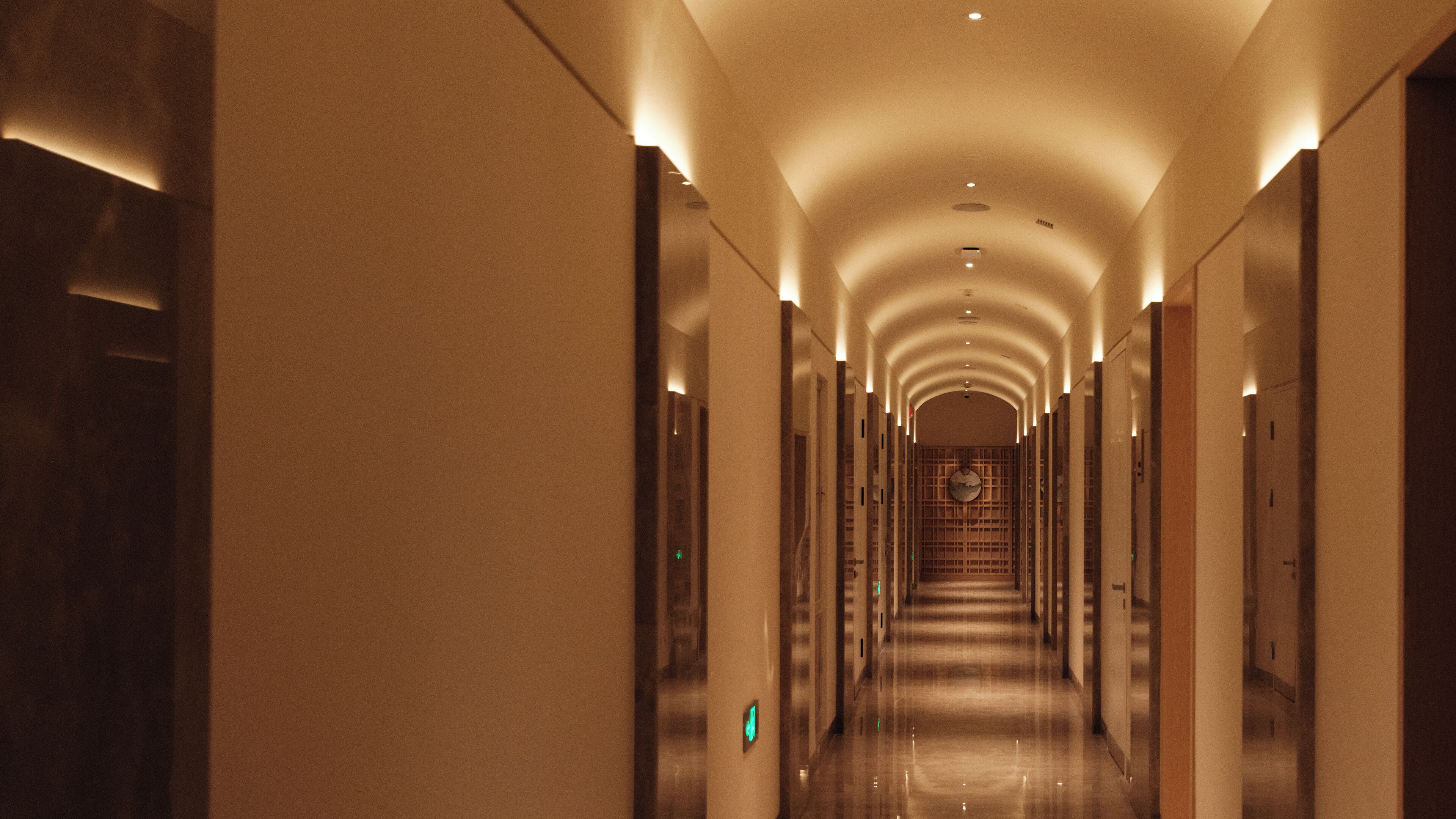 A long, well-lit corridor with a series of doors on either side, leading to a staircase at the end.