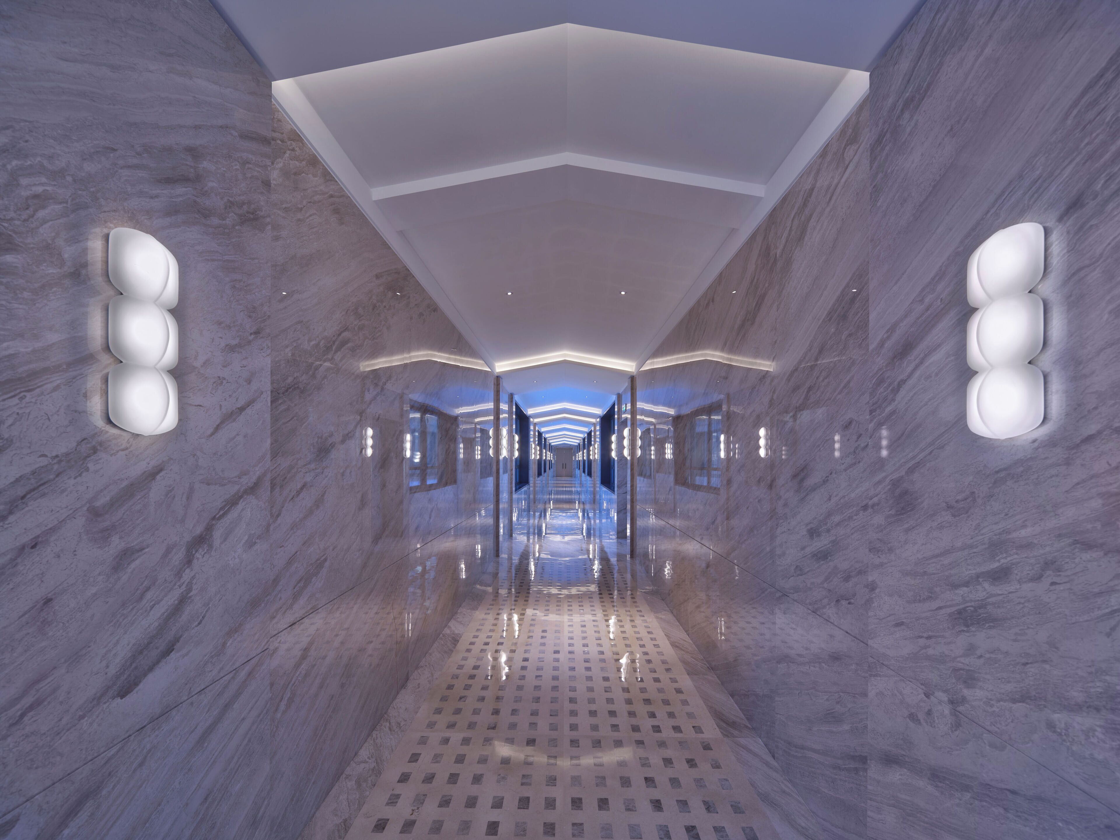 A modern, well-lit hallway with marble walls and a reflective floor, leading to a bright, open space.