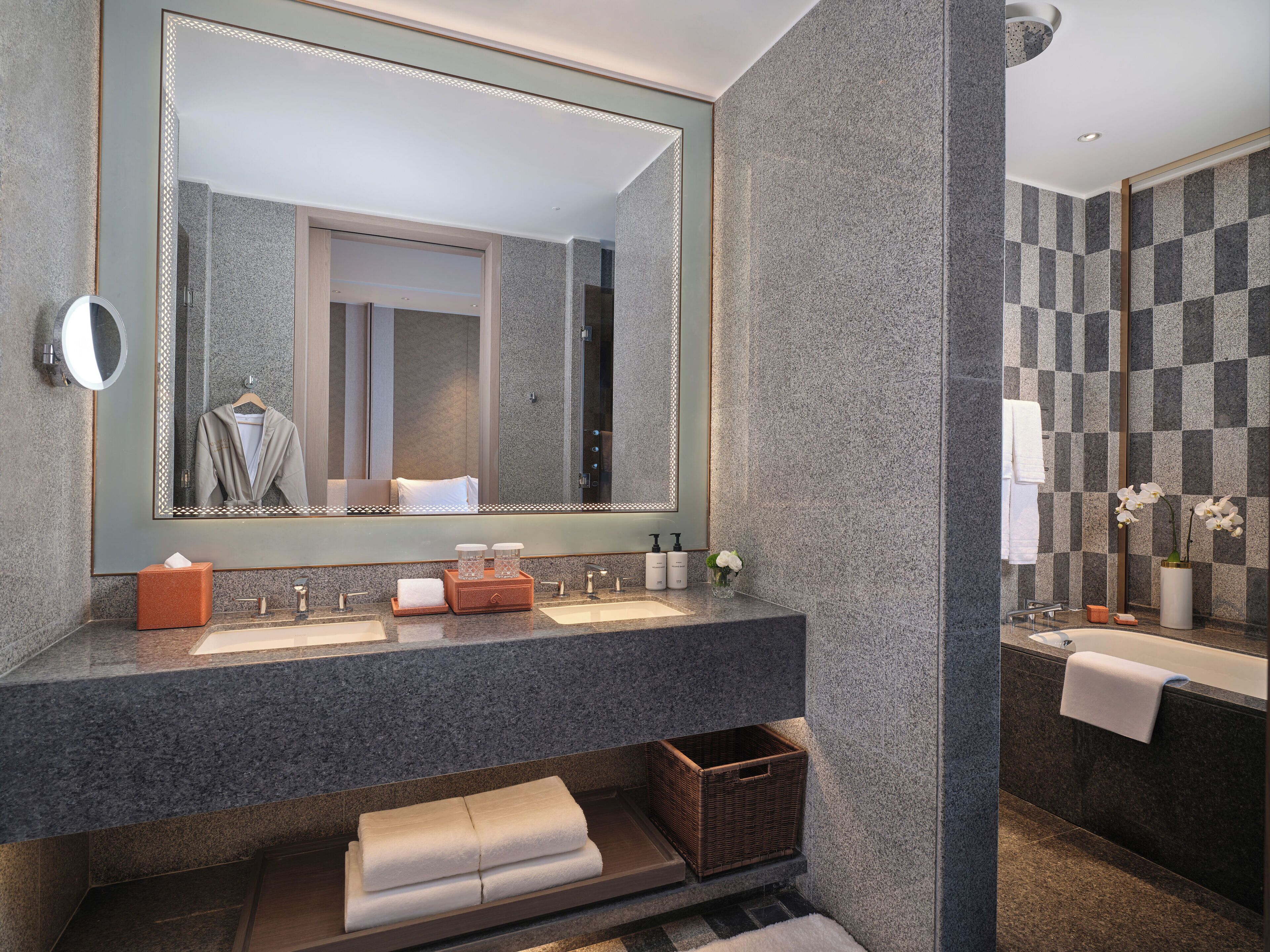 Un baño moderno con un espejo grande, dos lavamanos, una bañera y una pequeña cesta de mimbre.