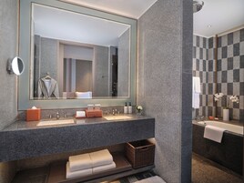 Un baño moderno con un espejo grande, dos lavamanos, una bañera y una pequeña cesta de mimbre.
