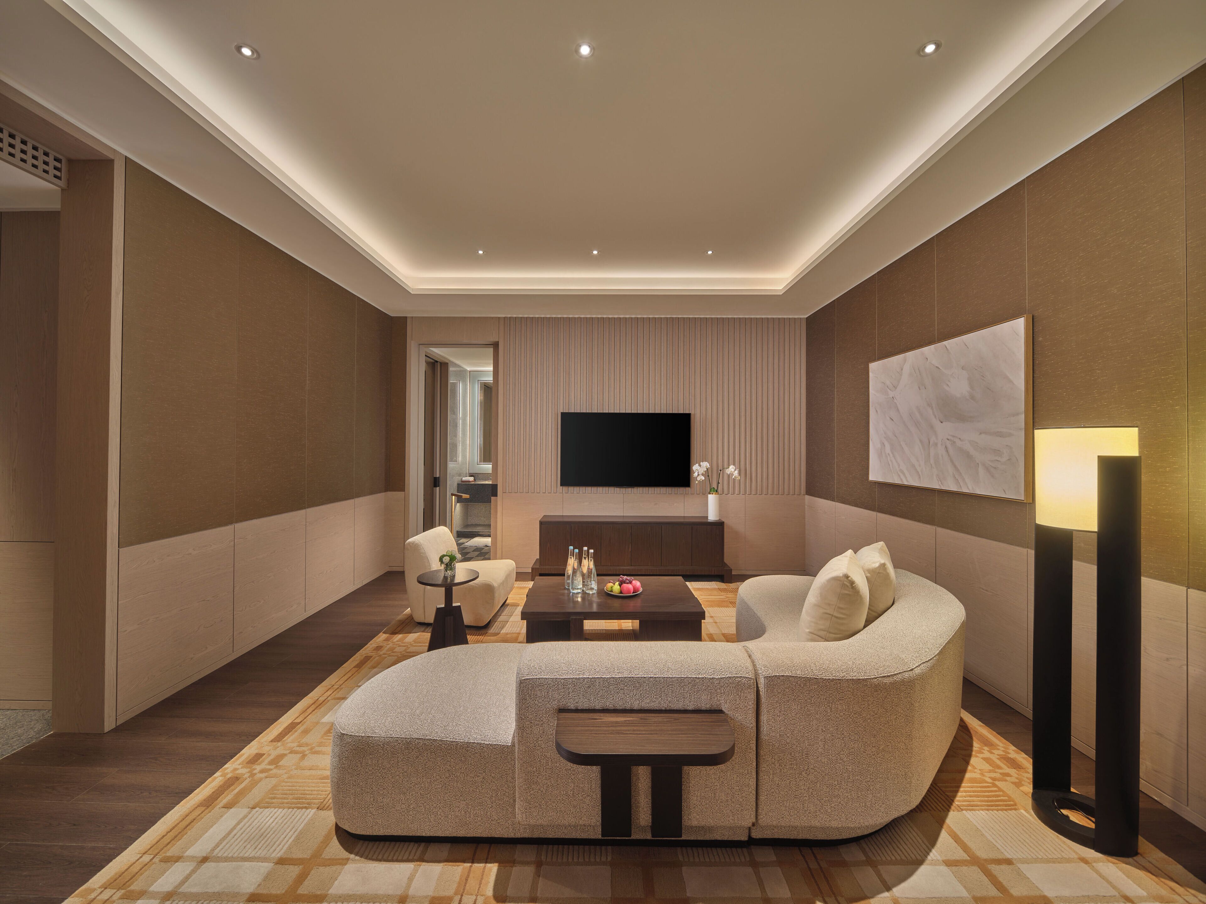 A modern living room with a curved sofa, a flat-screen TV, a coffee table, and a floor lamp.