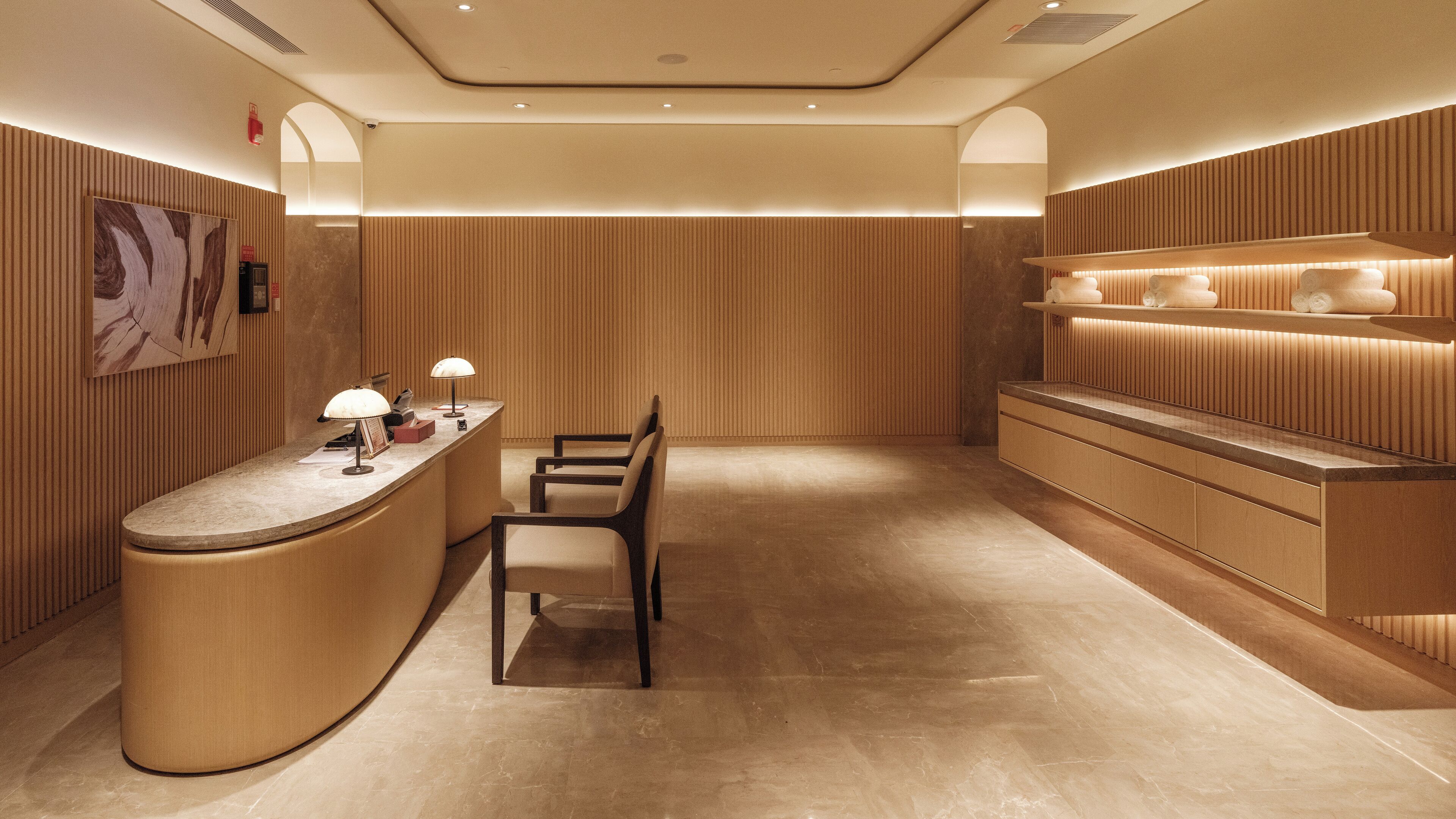 A modern reception area with a curved counter, a chair, and a shelf with towels.