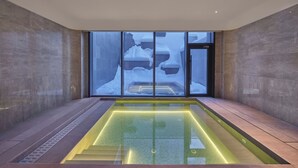 A modern indoor pool area with a glass wall providing a view of a snowy outdoor scene. - Conrad Altay Hemu (Burqin)