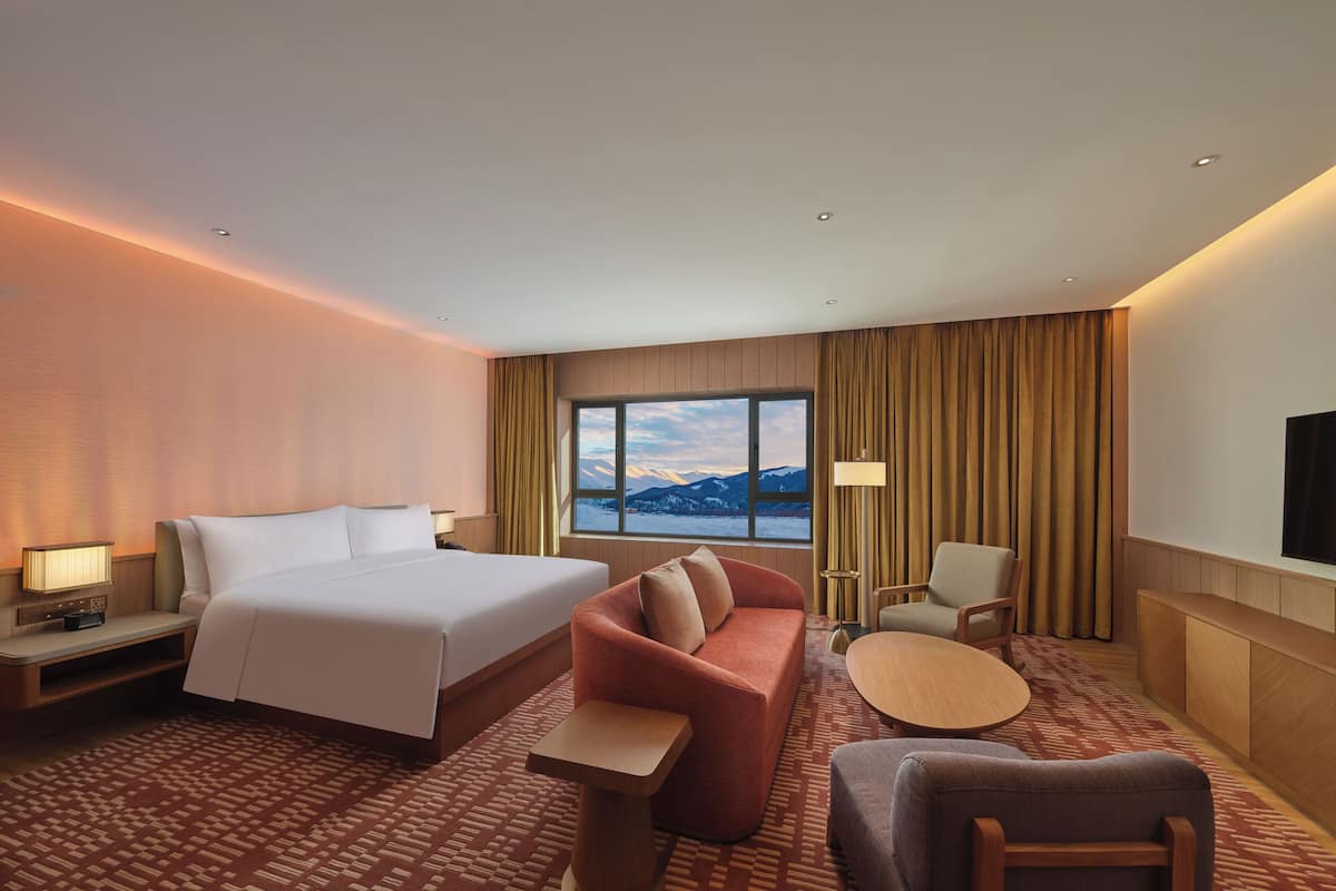 A hotel room with a large bed, a sofa, a small table, and a TV on the wall.