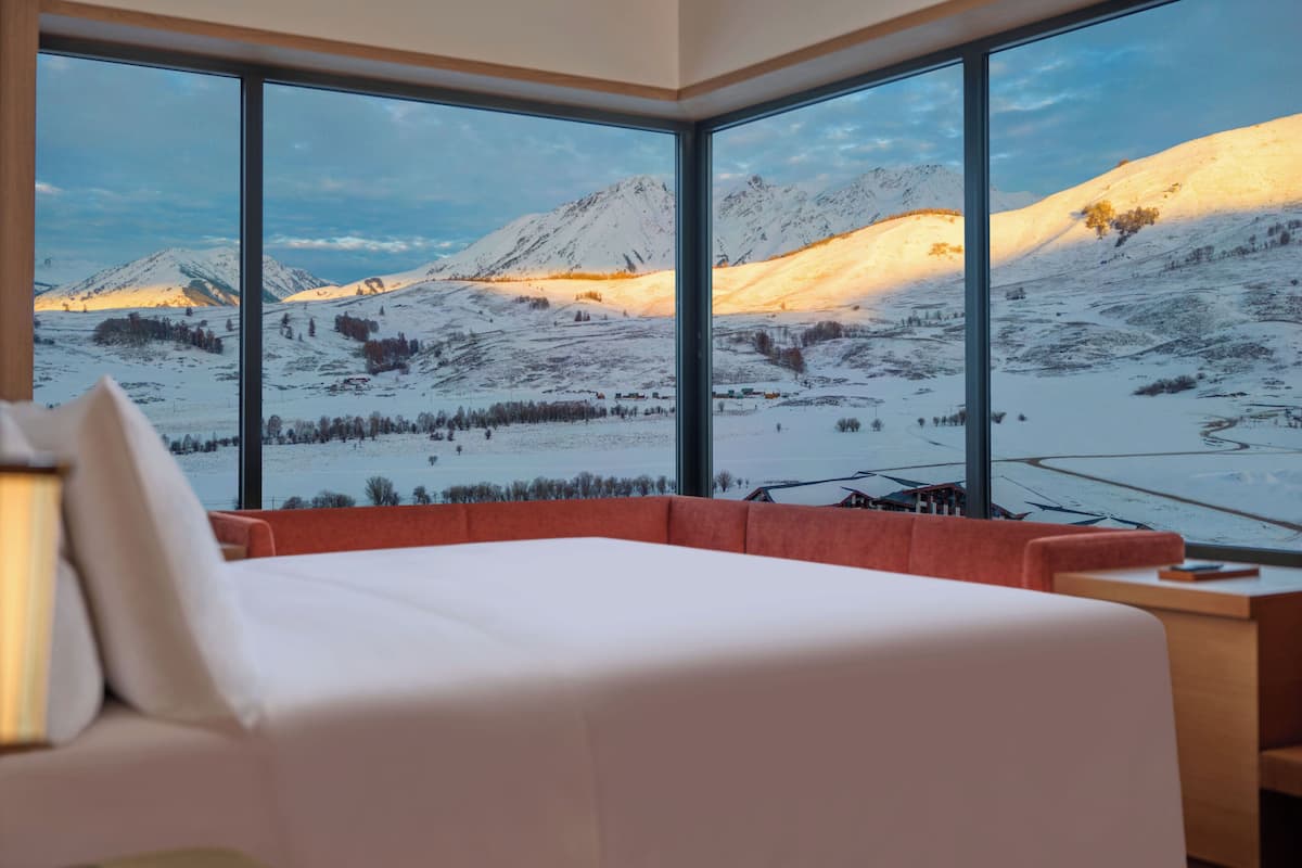 A bedroom with a large window offering a view of snow-covered mountains.