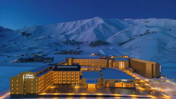 A large, modern hotel complex with multiple buildings, surrounded by snow-covered mountains. - Hilton Altay Hemu (Burqin)