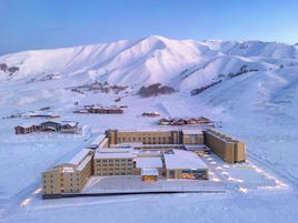 Un hotel cubierto de nieve con varias edificaciones, un estacionamiento y una pista de esquí al fondo.