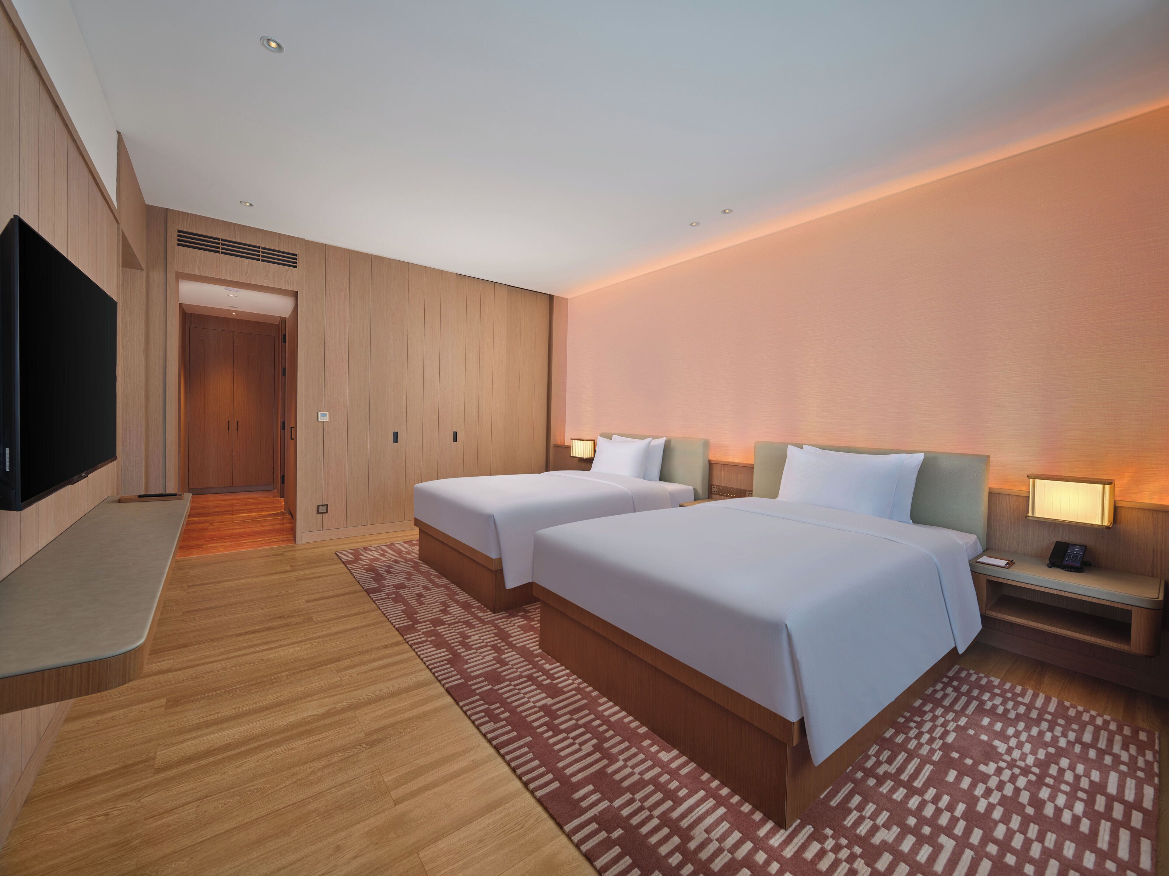 A hotel room with two beds, a TV, a desk, and a bathroom.