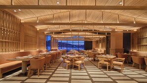 A spacious dining area with wooden tables and benches, large windows offering a view of the outdoors, and a high ceiling with wooden beams. - Hilton Altay Hemu (Burqin)