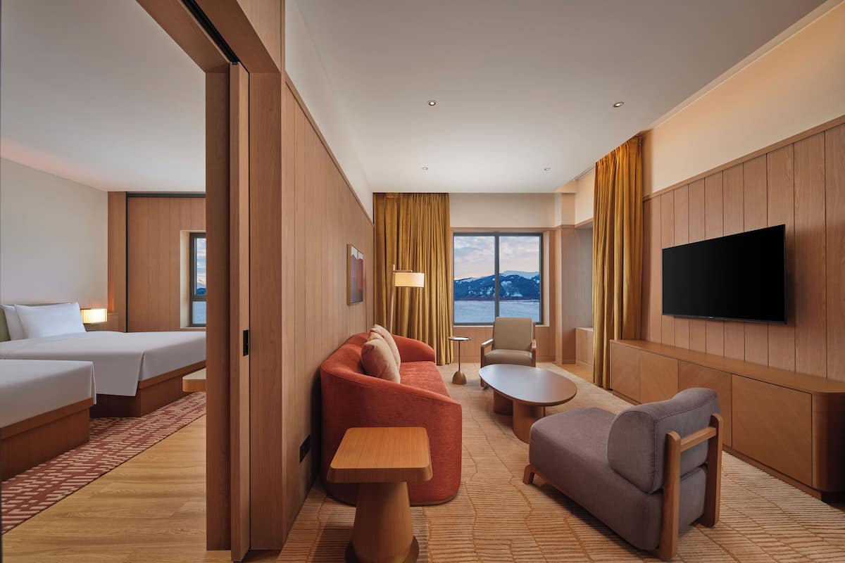 A hotel room with a bed, sofa, armchair, small table, and a TV mounted on the wall.