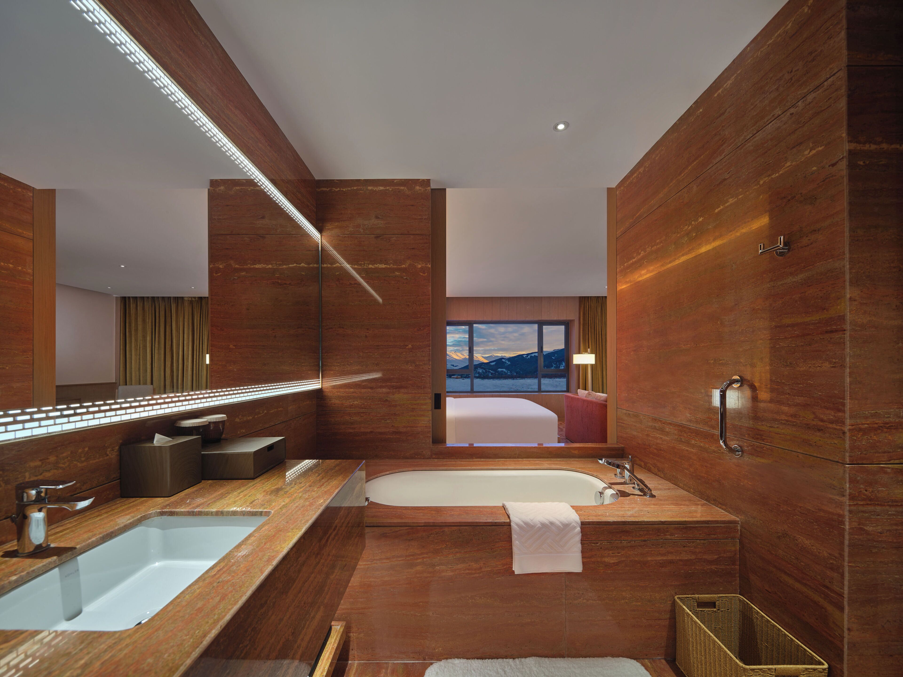 Un baño moderno con un espejo grande, lavamanos dobles, una bañera y vistas a las montañas a través de un amplio ventanal.