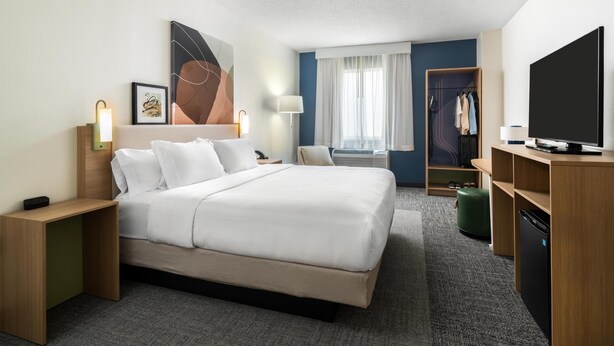 Een hotelkamer met een groot bed, nachtkastjes, een televisie, een kledingkast en een raam met gordijnen.
