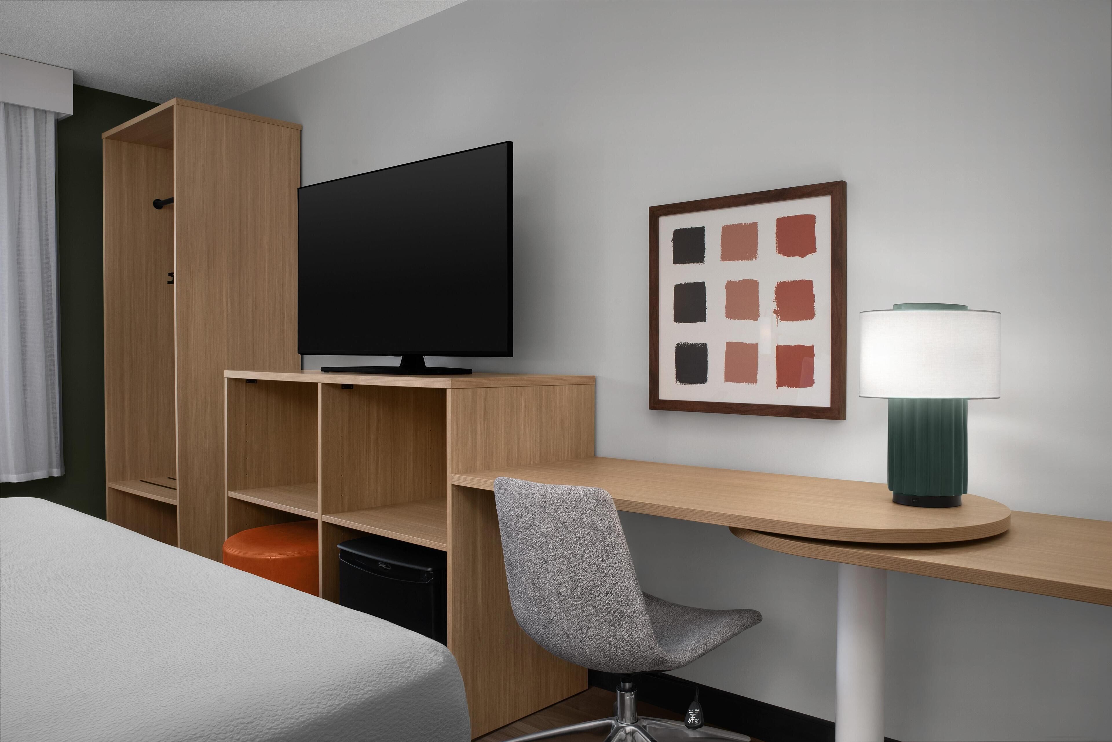 Habitación de hotel con una cama, un escritorio con silla, un televisor y una lámpara.
