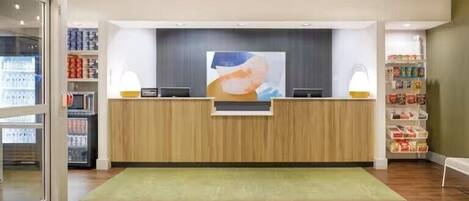 A reception desk with a wooden finish, a large abstract painting above it, and a green rug in front.