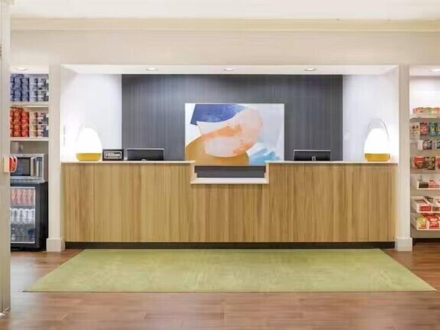 A reception desk with a wooden finish, a large abstract painting above it, and a green rug in front.