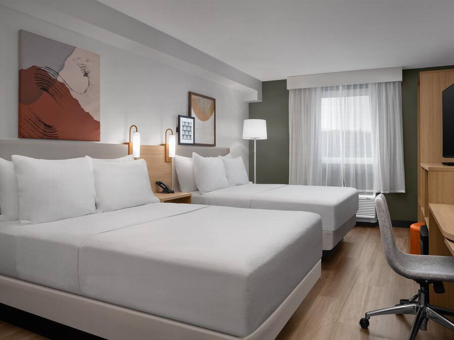 Habitación de hotel con dos camas, un escritorio, una silla, un televisor y una ventana con cortinas.
