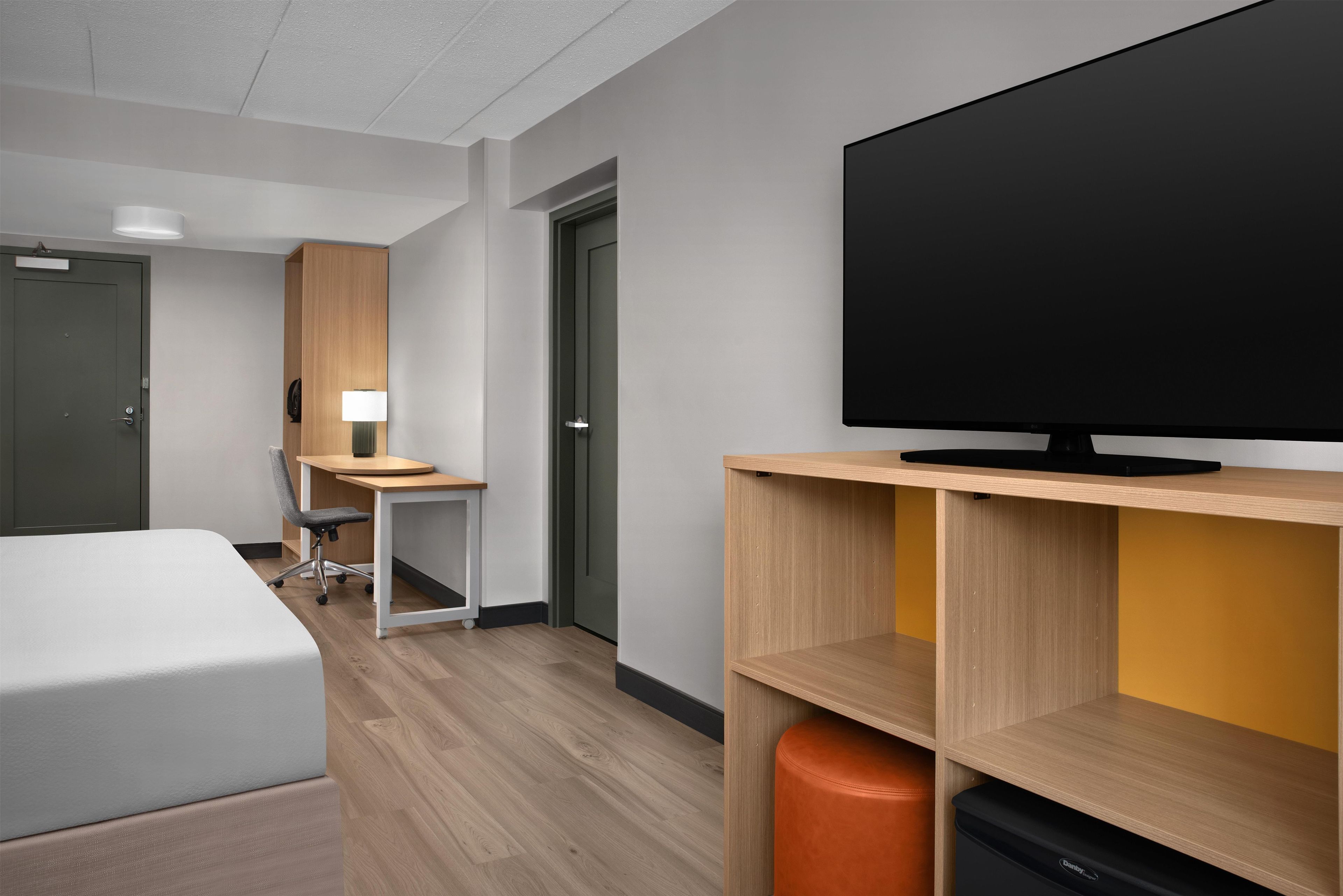 A hotel room with a bed, desk, chair, television, and storage unit.