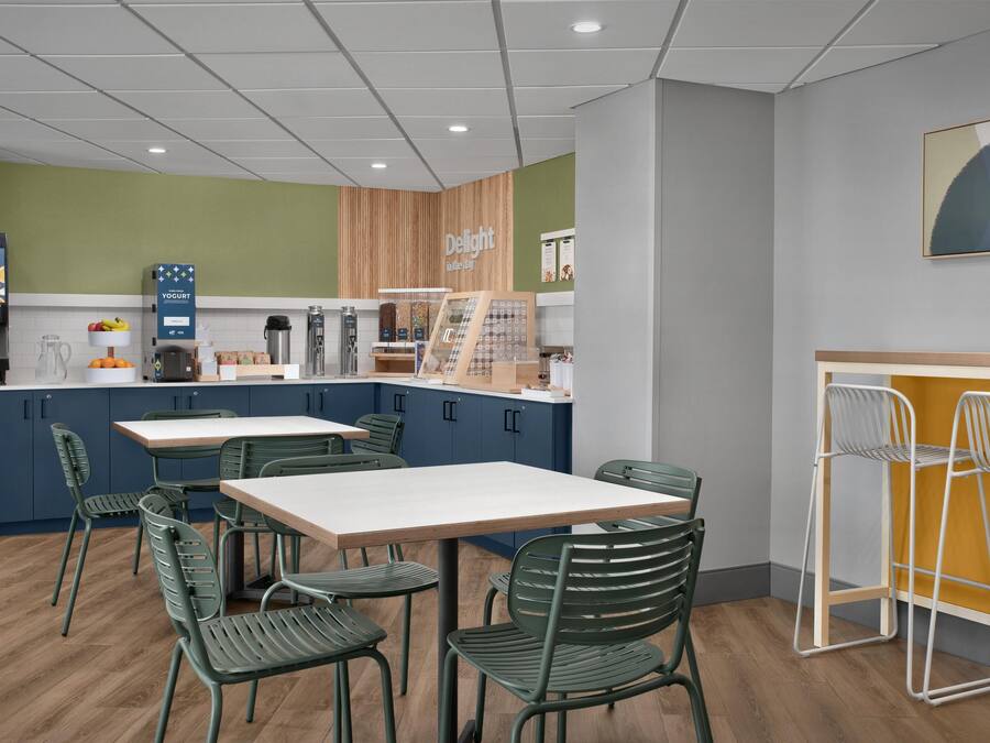 Un café moderno con mostrador de madera, sillas verdes y una mesa blanca.