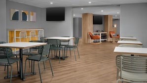 Een moderne vergaderruimte met meerdere tafels en stoelen, een groot flatscreen televisietoestel en een houten scheidingswand.