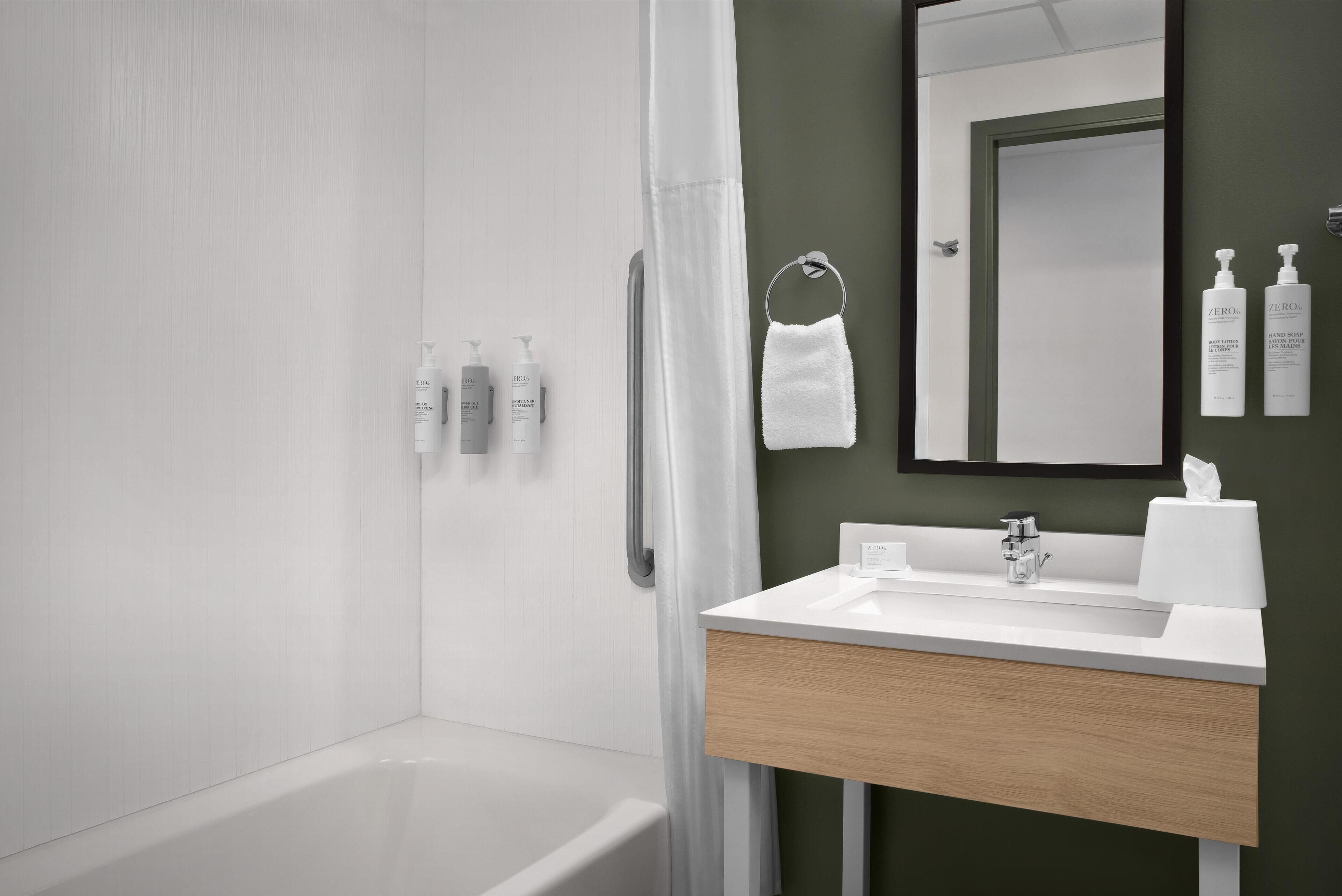 Une salle de bain moderne avec une baignoire, un lavabo avec un miroir et des articles de toilette fixés au mur.