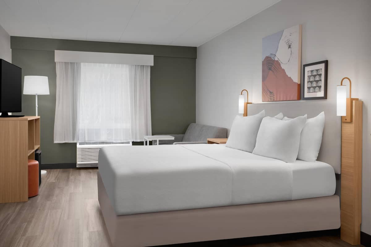 Een moderne hotelkamer met een groot bed, een bureau, een stoel, een televisie en een raam met gordijnen.