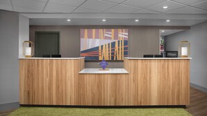Een receptiebalie van een hotel met een modern design, afgewerkt met hout en een kleurrijk abstract kunstwerk erboven.