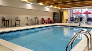 Une piscine intérieure avec des poutres en bois, des chaises longues et un parasol.