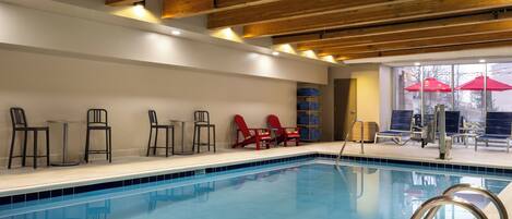 Una piscina interior con vigas de madera, sillones de descanso y una sombrilla.