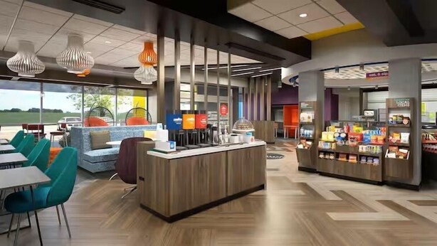 Un hall d'hôtel moderne doté d'un comptoir d'accueil central, d'un espace détente avec des canapés et des fauteuils, et d'un kiosque en libre-service.