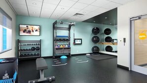 Une salle de sport moderne équipée de matériel d’exercice, d’un téléviseur fixé au mur et d’un miroir.