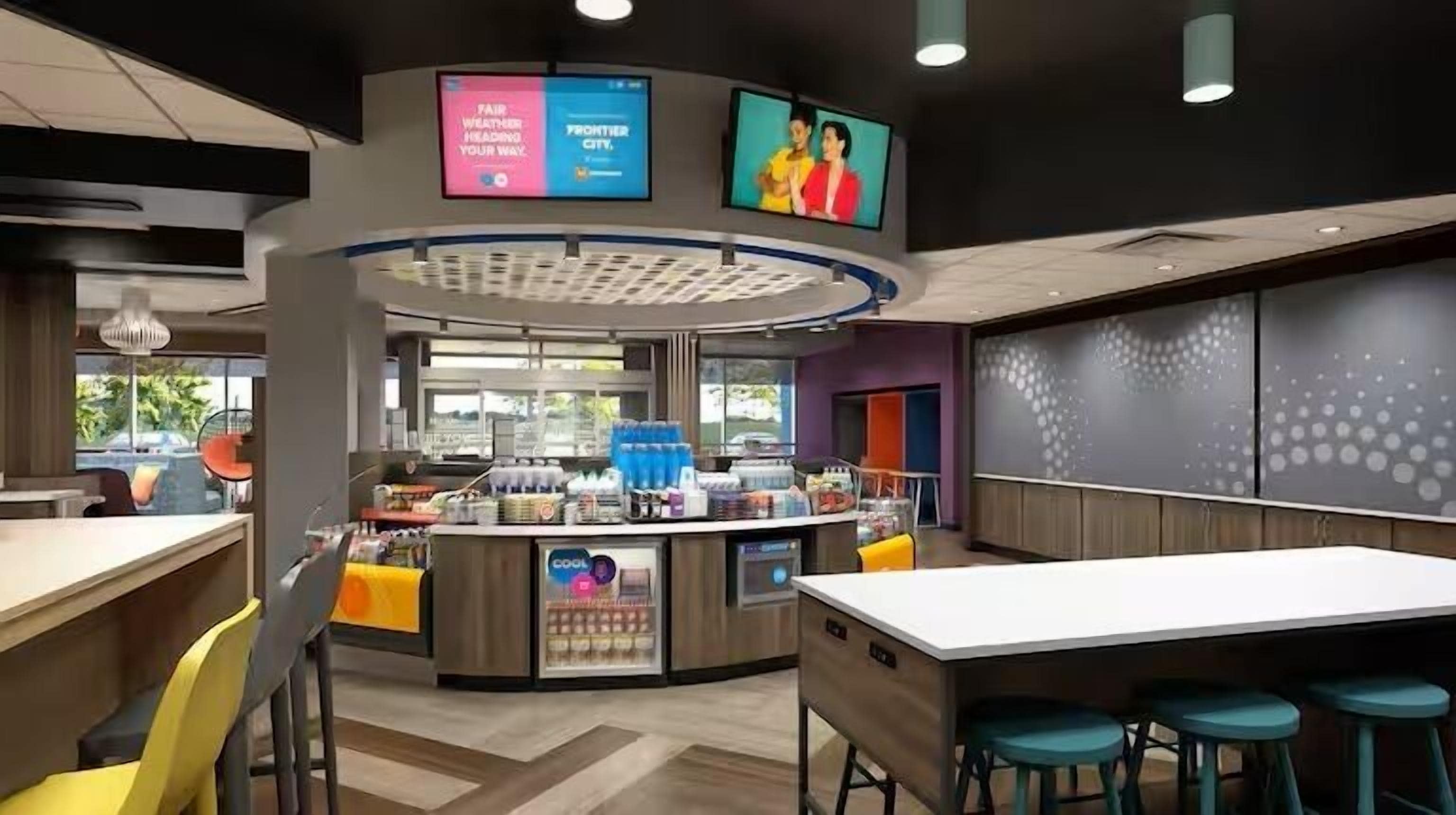 A modern cafe with a central counter, seating area, and two digital screens displaying advertisements.